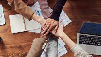Diverse office team stacks hands over a conference table